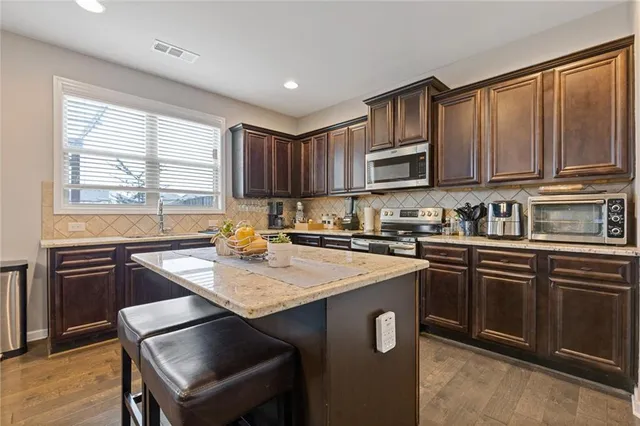 a kitchen with stainless steel appliances granite countertop a stove a sink dishwasher a microwave oven and a refrigerator with wooden cabinets