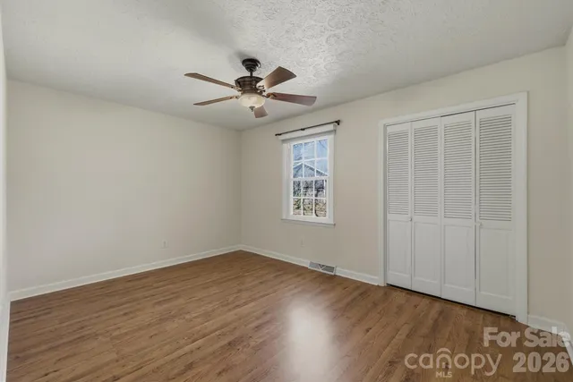 an empty room with wooden floor chandelier fan and windows