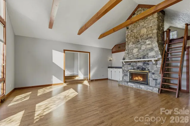a view of an empty room with wooden floor fireplace and a window