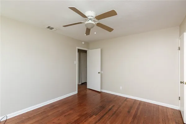 an empty room with wooden floor ceiling fan and windows