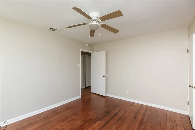 an empty room with wooden floor ceiling fan and windows