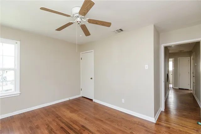 an empty room with wooden floor fan and windows