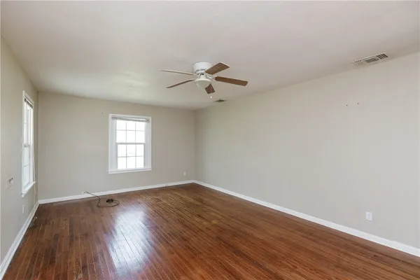 an empty room with wooden floor windows and fan
