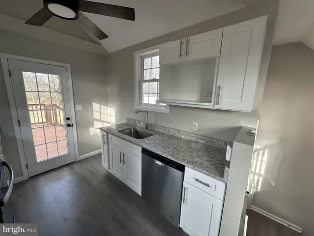 a kitchen with stainless steel appliances granite countertop a stove a sink and white cabinets with wooden floor next to windows