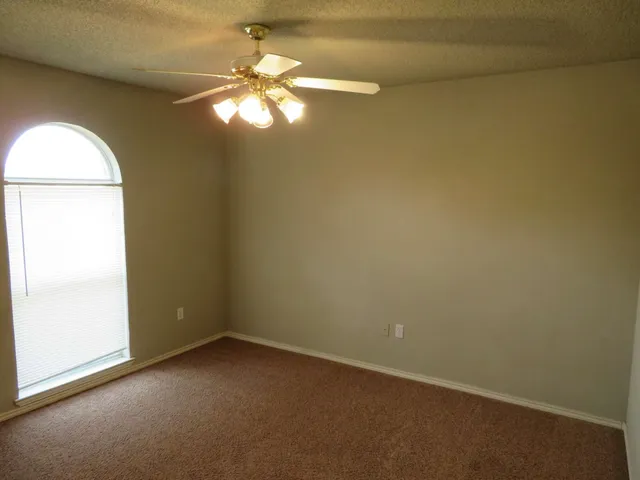 an empty room with a chandelier fan and windows