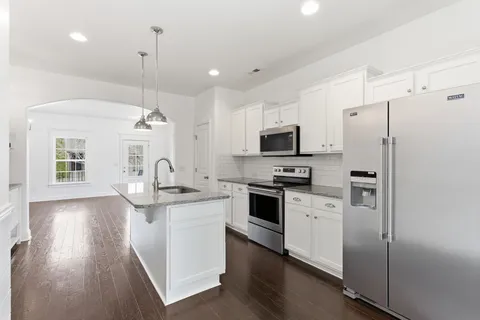 a kitchen with stainless steel appliances granite countertop a sink a stove a refrigerator and island with wooden floor