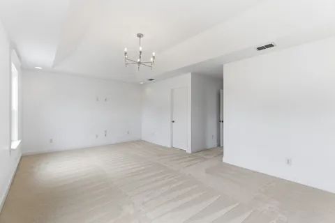 an empty room with a chandelier fan and wooden floor