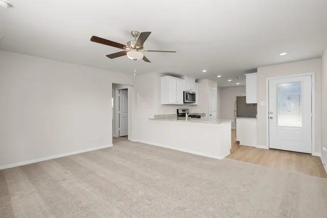 a view of an empty room with kitchen appliances and a ceiling fan