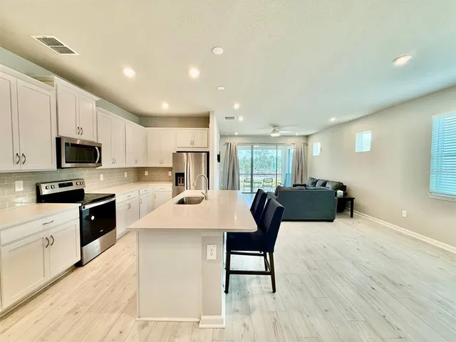 a large kitchen with stainless steel appliances kitchen island granite countertop a stove a sink a refrigerator and white cabinets with wooden floor