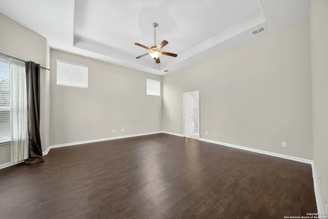 an empty room with wooden floor ceiling fan and windows