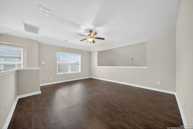 an empty room with wooden floor chandelier fan and windows