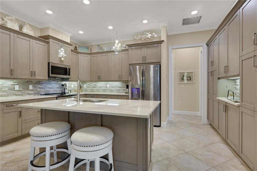 5752 Elbow Avenue Naples, FL 34113 - Photo 7 of 38 Kitchen featuring a kitchen island with sink, a breakfast bar area, light stone counters, stainless steel appliances, and backsplash