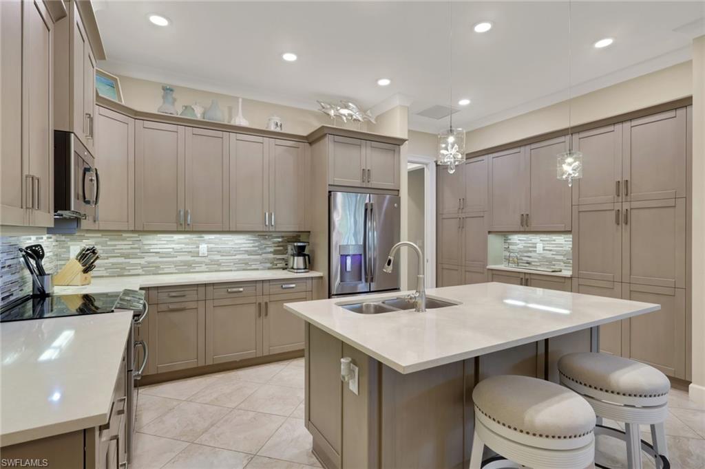 5752 Elbow Avenue Naples, FL 34113 - Photo 9 of 38 Kitchen with stainless steel appliances, a kitchen bar, a kitchen island with sink, pendant lighting, and light stone counters