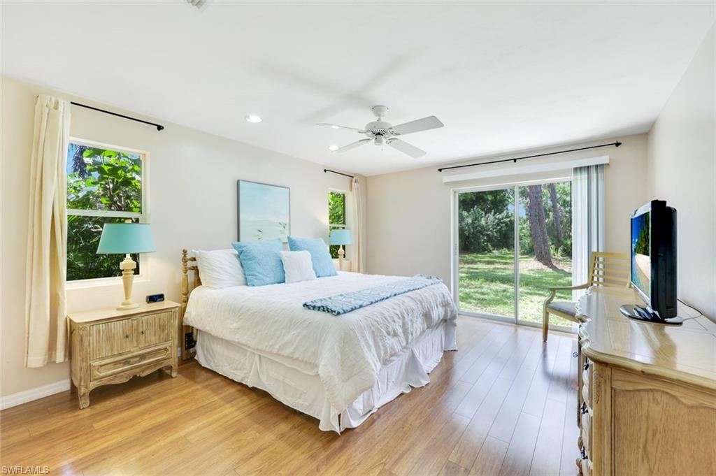 131 Cajeput Drive Naples, FL 34108 - Photo 14 of 30 a bedroom with a large bed and a flat tv screen on dresser with wooden floor