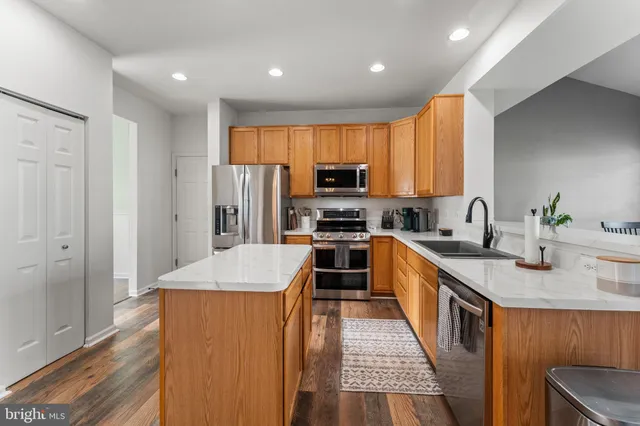 a kitchen with stainless steel appliances granite countertop a stove top oven a sink dishwasher and a refrigerator with wooden floor