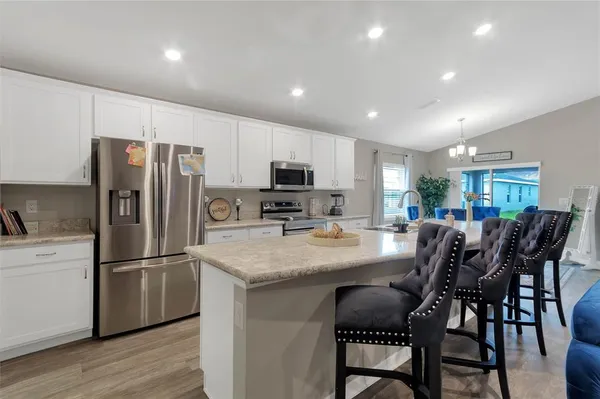a kitchen with stainless steel appliances granite countertop a dining table chairs refrigerator and microwave