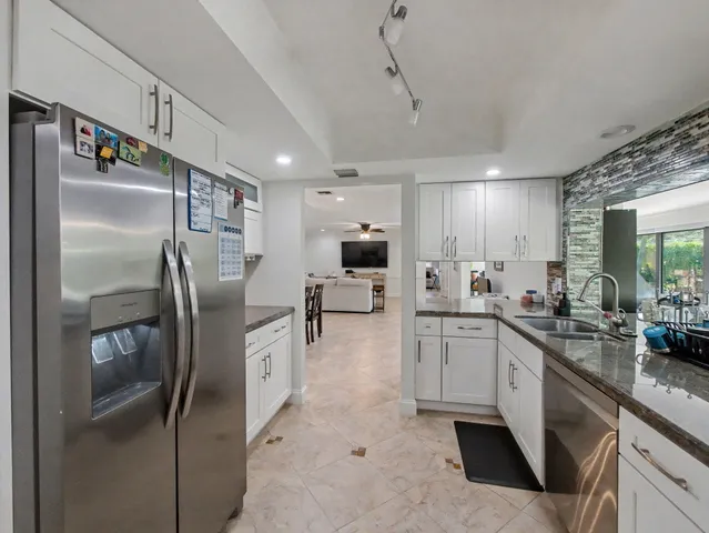 a kitchen with stainless steel appliances granite countertop a refrigerator a sink a stove and white cabinets