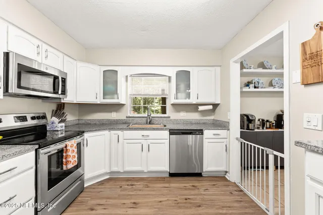 a kitchen with stainless steel appliances granite countertop a stove top oven a sink dishwasher and white cabinets with wooden floor