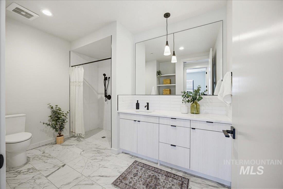 4184 East Haystack Street, Unit 103 Boise, ID 83716 - Photo 11 of 27 Spacious bathroom featuring marble-look floor tiling, a walk-in shower with black fixtures, and a dual-sink vanity with white cabinetry and a full-width mirror