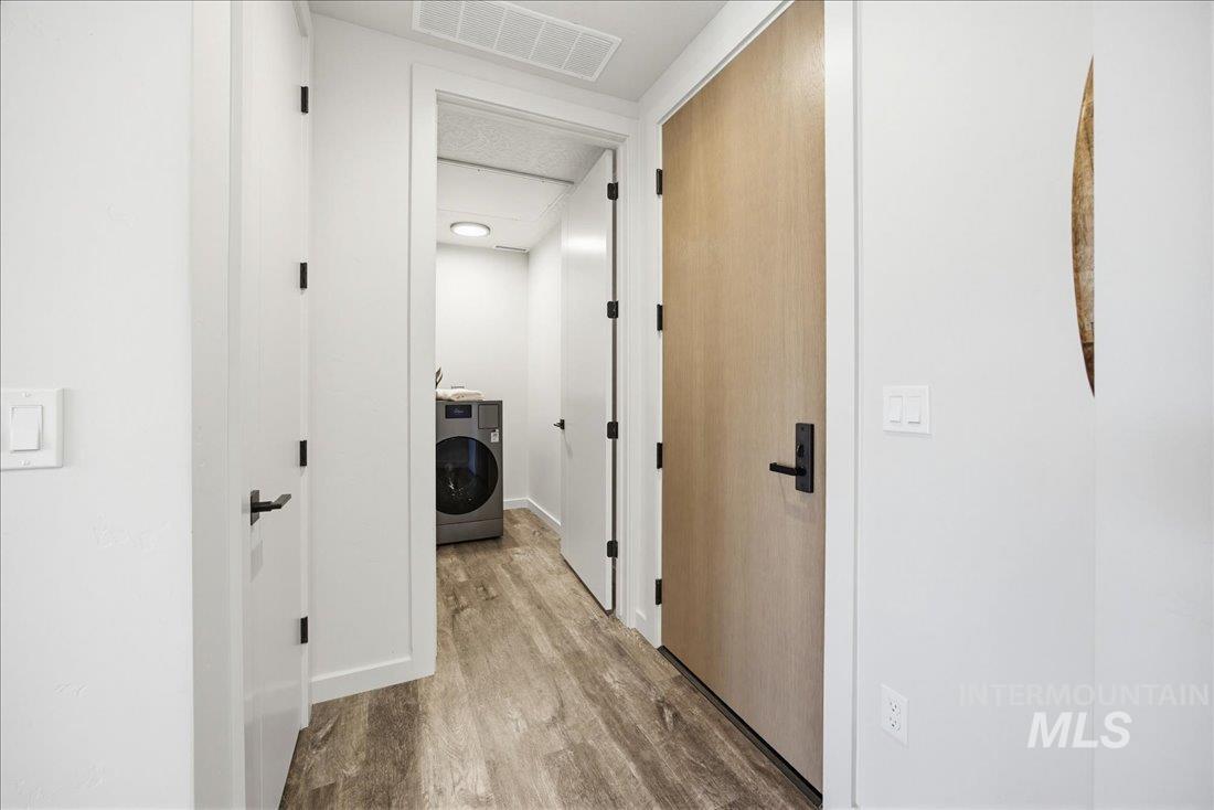 4184 East Haystack Street, Unit 103 Boise, ID 83716 - Photo 12 of 27 Hallway featuring wood-finish flooring, white walls, and a light wood-finish door with matte black hardware