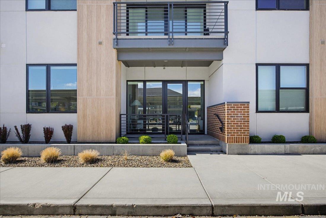 4184 East Haystack Street, Unit 103 Boise, ID 83716 - Photo 15 of 27 Modern building exterior featuring a ground-level entrance with glass doors, a second-story balcony with metal railings, and a wood-finish accent panel