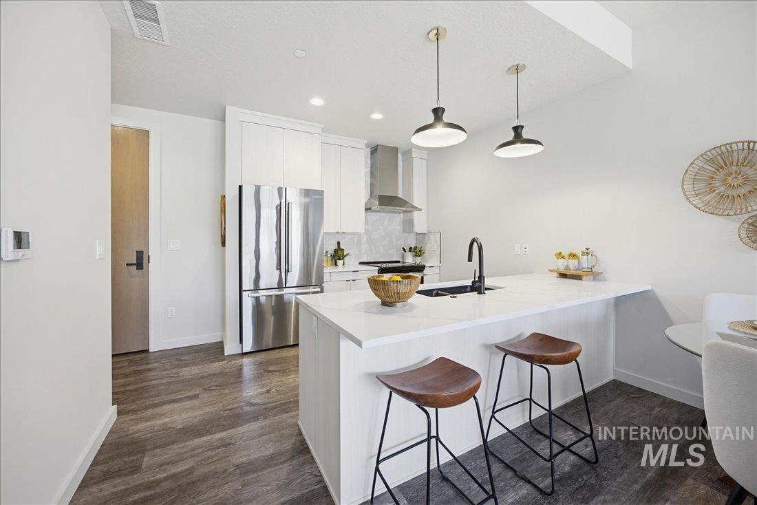 4184 East Haystack Street, Unit 103 Boise, ID 83716 - Photo 4 of 27 Open-concept kitchen featuring an island with white countertop, recessed lighting, wood-finish flooring, stainless steel appliances, and ceiling-mounted pendant lights