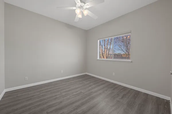 a view of an empty room with wooden floor and a ceiling fan