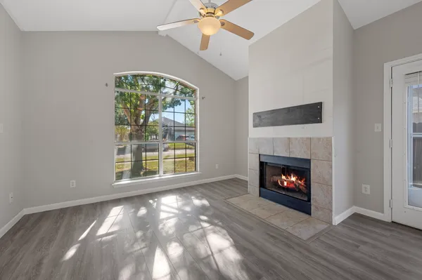 a view of an empty room with wooden floor fireplace and a window