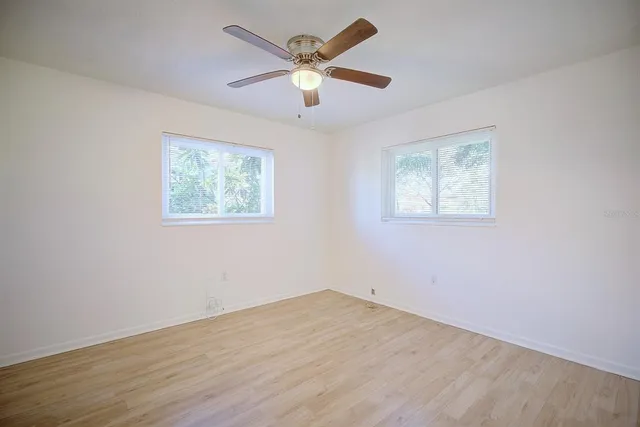 a view of an empty room with wooden floor and a ceiling fan