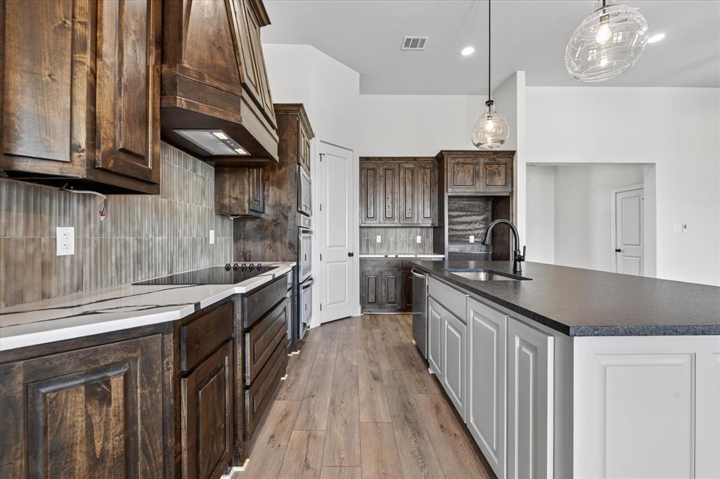 517 Longhorn Lane Springtown, TX 76082 - Photo 13 of 39 Kitchen featuring light wood-style floors, an island with sink, pendant lighting, two tone cabinetry, and decorative backsplash