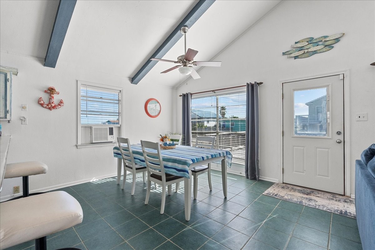 324 Shark Lane Surfside Beach, TX 77541 - Photo 12 of 49 Bright dining area with high ceilings and exposed beams, featuring a large window and door leading to a deck. The space has a coastal vibe with nautical decor and a striped tablecloth.