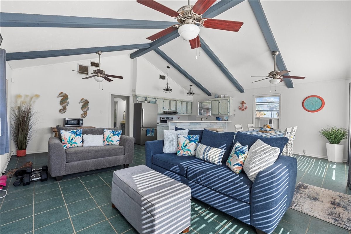 324 Shark Lane Surfside Beach, TX 77541 - Photo 13 of 49 Bright and airy open-concept living space with vaulted ceilings and exposed beams. Features include modern ceiling fans, cozy seating, and a seamless flow into a charming kitchen and dining area. Ideal for relaxed living and entertaining.