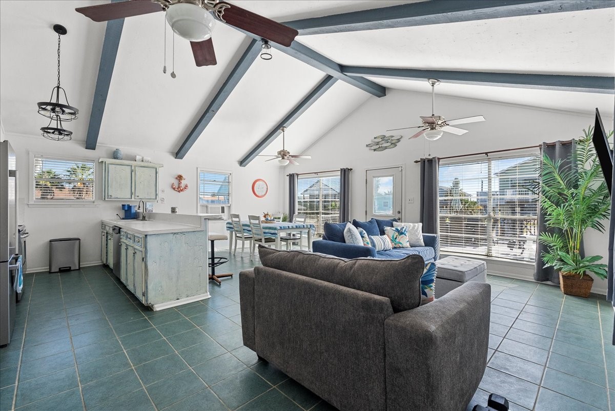 324 Shark Lane Surfside Beach, TX 77541 - Photo 16 of 49 Bright and spacious open-concept living area with high vaulted ceilings and exposed beams. Features a cozy seating area, dining space, and a kitchen with rustic cabinetry. Large windows provide ample natural light and views, enhancing the airy, welcoming atmosphere.