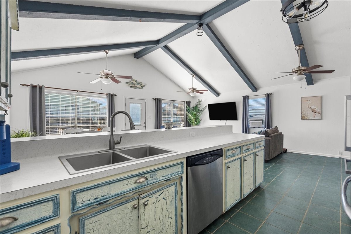 324 Shark Lane Surfside Beach, TX 77541 - Photo 19 of 49 This open-concept kitchen and living area features high vaulted ceilings with exposed beams, a large island with a double sink, and rustic cabinets. Natural light floods in through large windows and a glass door, enhancing the spacious feel. Ceiling fans and a wall-mounted TV add comfort and modern convenience.