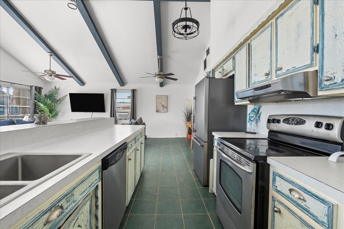 324 Shark Lane Surfside Beach, TX 77541 - Photo 20 of 49 This kitchen features a rustic charm with distressed cabinets, modern appliances, and a spacious layout. The vaulted ceiling with exposed beams adds character, while ceiling fans and a large window provide light and airflow.