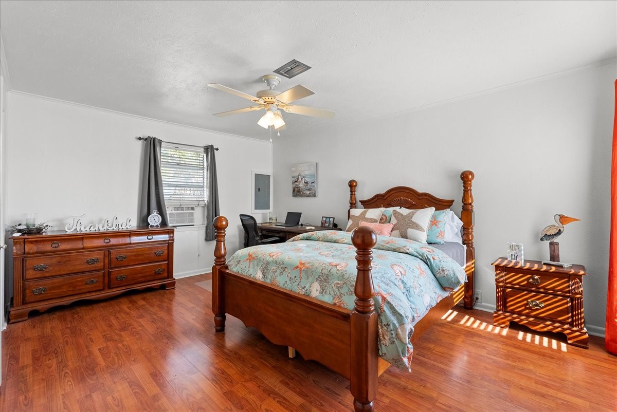 324 Shark Lane Surfside Beach, TX 77541 - Photo 21 of 49 This inviting bedroom features warm wooden flooring and a classic wooden bed frame. It includes a matching dresser and nightstand, a ceiling fan, and a window allowing natural light. The decor is cozy and stylish, creating a comfortable atmosphere.