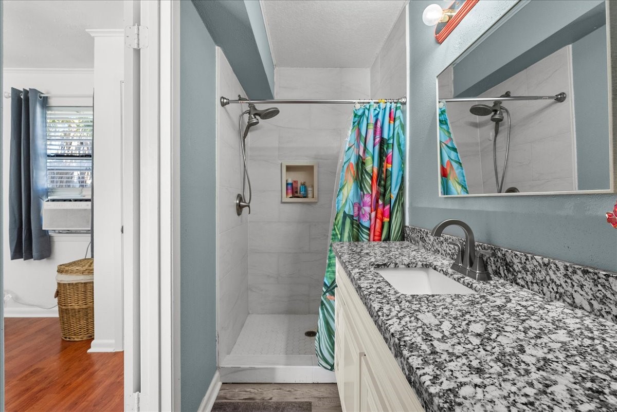 324 Shark Lane Surfside Beach, TX 77541 - Photo 25 of 49 This photo showcases a modern bathroom with a granite countertop and single sink vanity. It features a shower with a vibrant floral curtain and built-in shelving. The room has a clean, fresh look with natural light from an adjacent window.