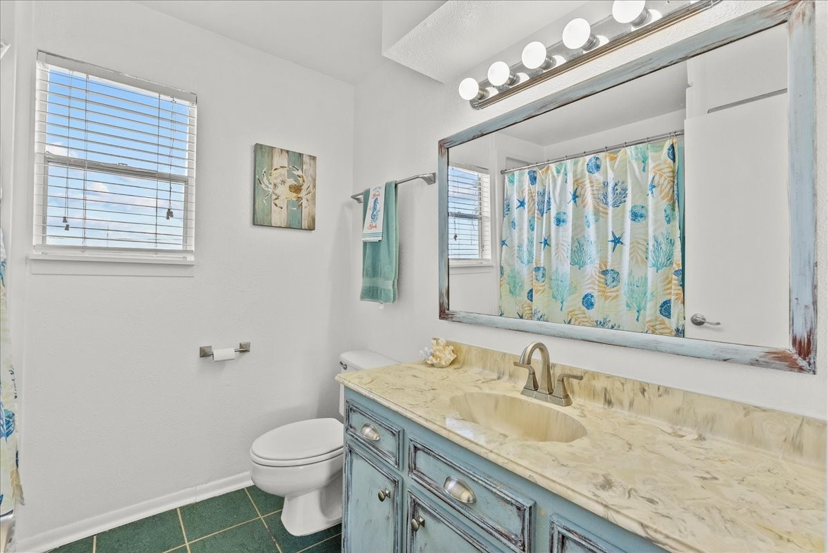 324 Shark Lane Surfside Beach, TX 77541 - Photo 28 of 49 Bright bathroom with a coastal theme, featuring a large mirror, updated countertop, and ocean-inspired shower curtain. Natural light streams through the windows, highlighting the decorative accents.