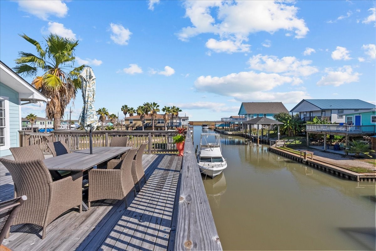 324 Shark Lane Surfside Beach, TX 77541 - Photo 33 of 49 This waterfront property features a spacious deck with outdoor seating, overlooking a serene canal. Perfect for boating enthusiasts, it includes a boat dock and offers picturesque views of neighboring homes and palm trees.