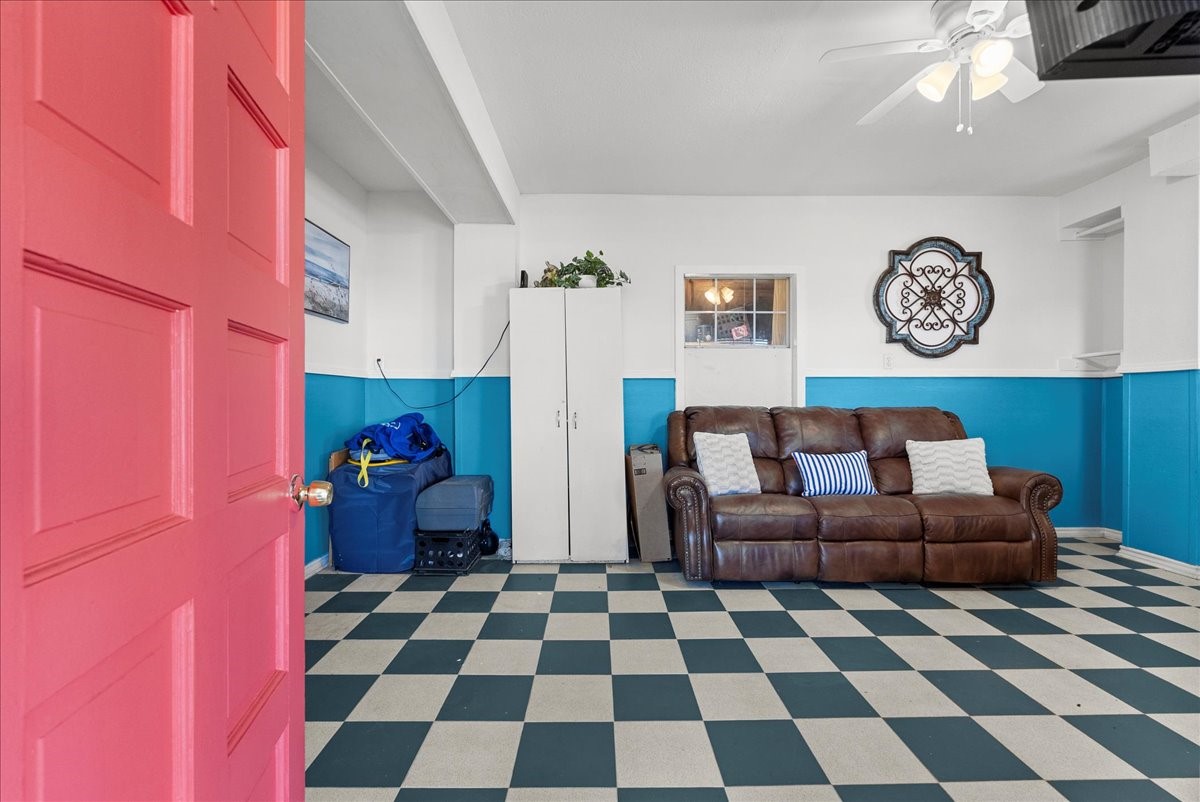 324 Shark Lane Surfside Beach, TX 77541 - Photo 34 of 49 This room features a vibrant painted door and a cozy setup with a brown leather sofa. It has a checkered tile floor, white upper walls with a blue accent, and a ceiling fan. Storage cabinets and decorative wall elements add functionality and charm.