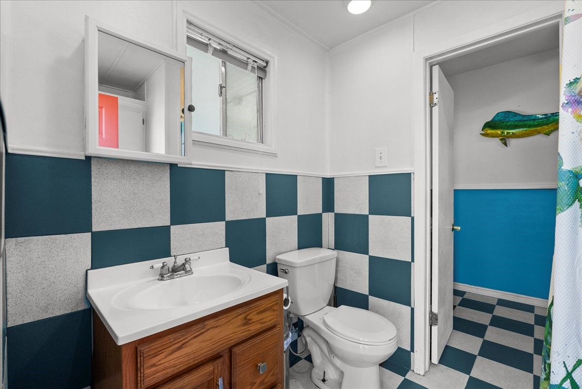 324 Shark Lane Surfside Beach, TX 77541 - Photo 37 of 49 This bathroom features a distinctive checkered tile design, a wooden vanity with a white sink, and a wall-mounted mirror. The window provides natural light, and the space has a fresh, colorful look.