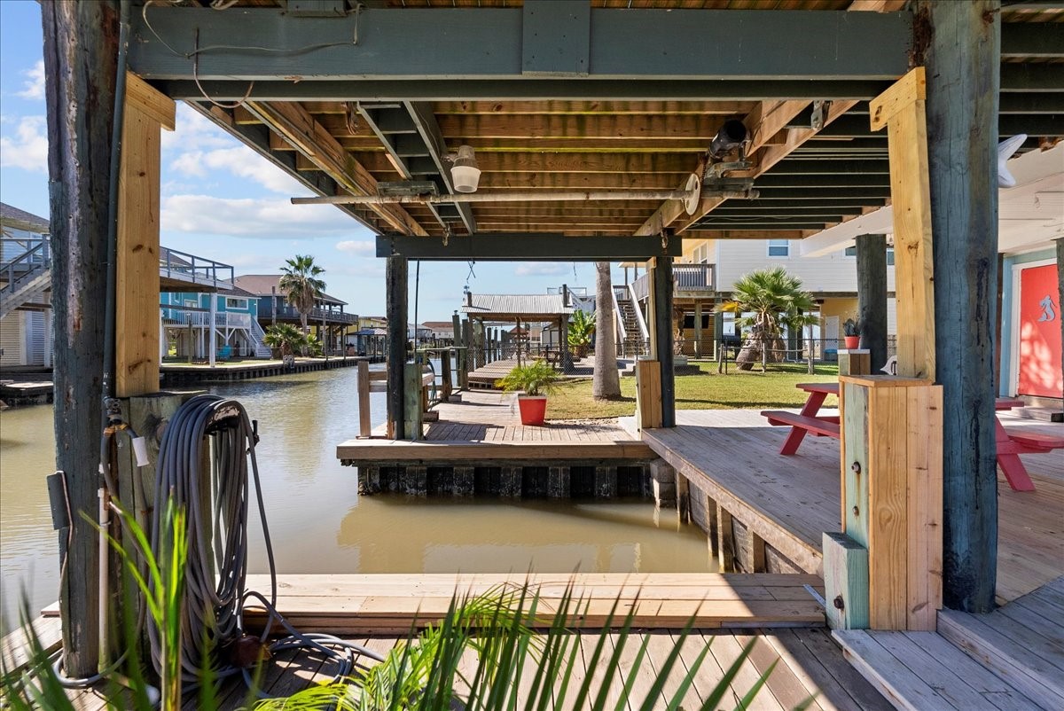 324 Shark Lane Surfside Beach, TX 77541 - Photo 40 of 49 This photo showcases a charming waterfront property with a covered dock and canal access. The outdoor space includes a wooden deck and a picnic table, perfect for relaxing and enjoying the view. The area is lined with palm trees and offers direct water access for boating or fishing enthusiasts.