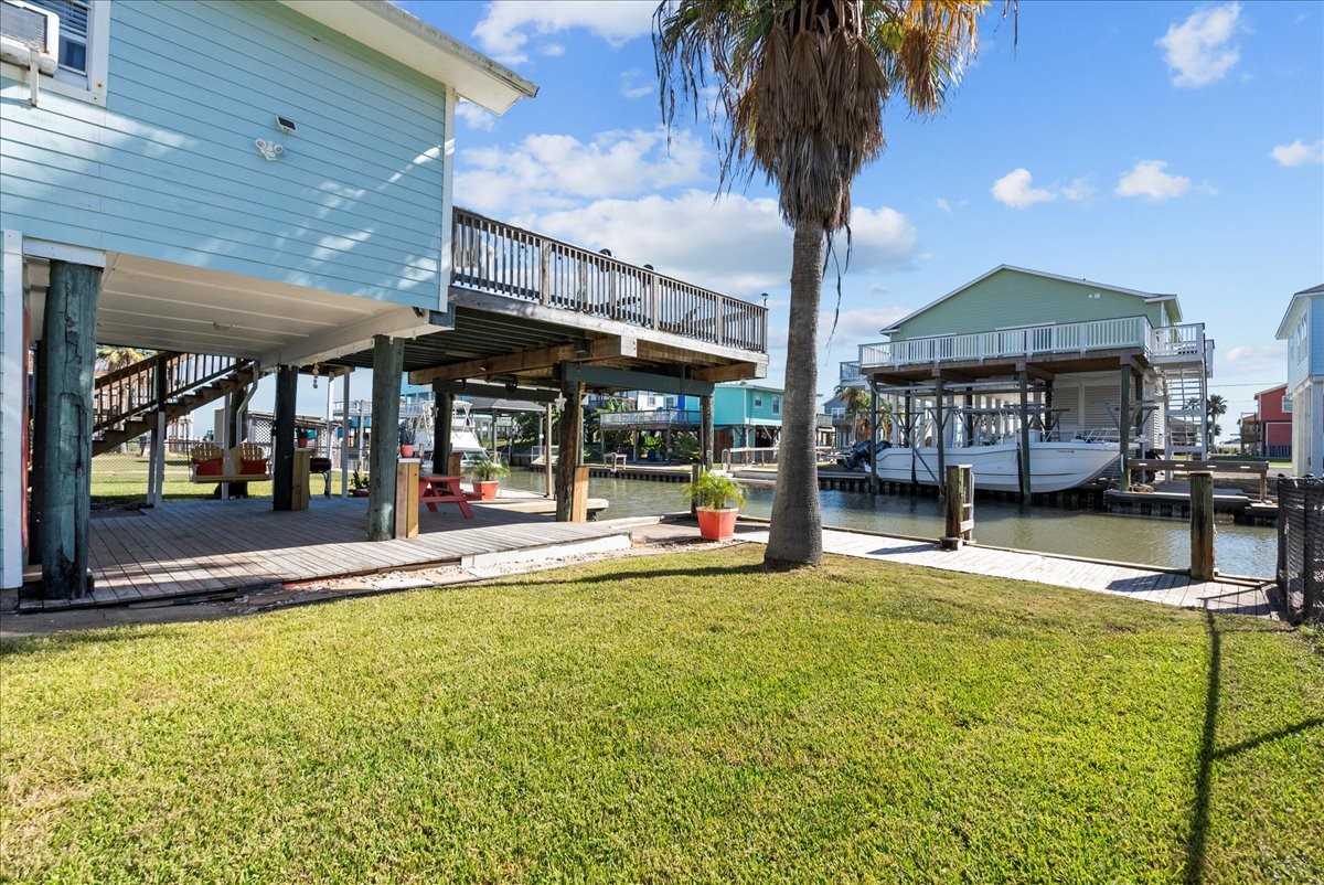 324 Shark Lane Surfside Beach, TX 77541 - Photo 42 of 49 This waterfront property features a raised coastal home with a spacious deck overlooking a canal. The yard is landscaped with grass and a palm tree, offering a relaxing outdoor space. Ideal for boating enthusiasts, with dock access nearby.