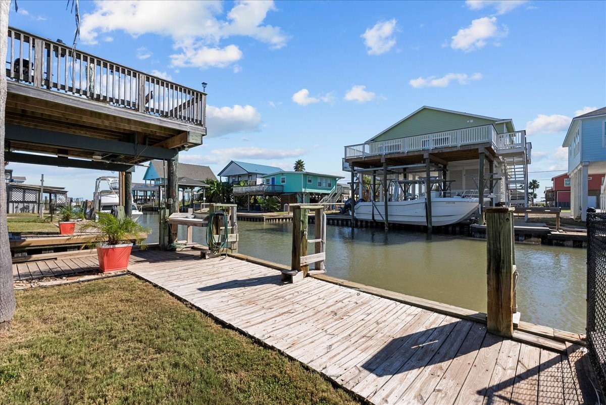 324 Shark Lane Surfside Beach, TX 77541 - Photo 43 of 49 This photo showcases a waterfront property with a wooden dock and a boat slip The area features a canal view, neighboring houses with elevated decks, and a well-maintained lawn with potted plants, perfect for boating enthusiasts.