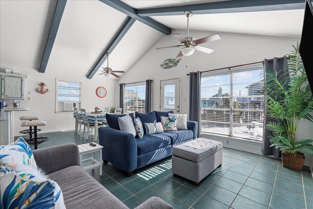 324 Shark Lane Surfside Beach, TX 77541 - Photo 10 of 49 This bright living space features high vaulted ceilings with exposed beams, large windows for natural light, and a cozy seating area. The open layout includes a dining area and a well-equipped kitchen. The décor is modern with coastal accents, and the space feels airy and inviting.