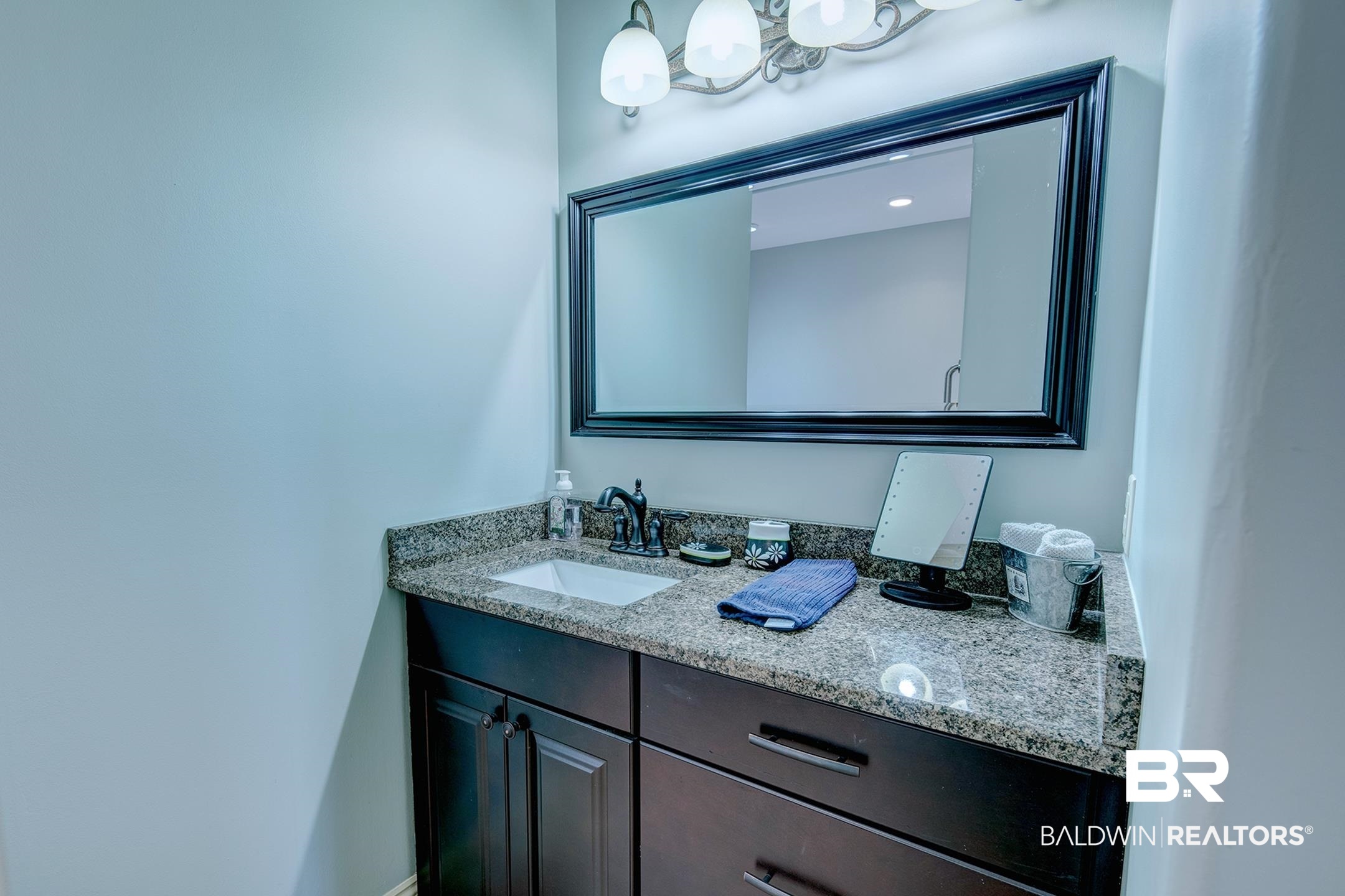 9357 Lakeview Drive Foley, AL 36535 - Photo 60 of 68 Dark wood-finish vanity with an undermount sink, speckled countertop, and wall-mounted light fixture
