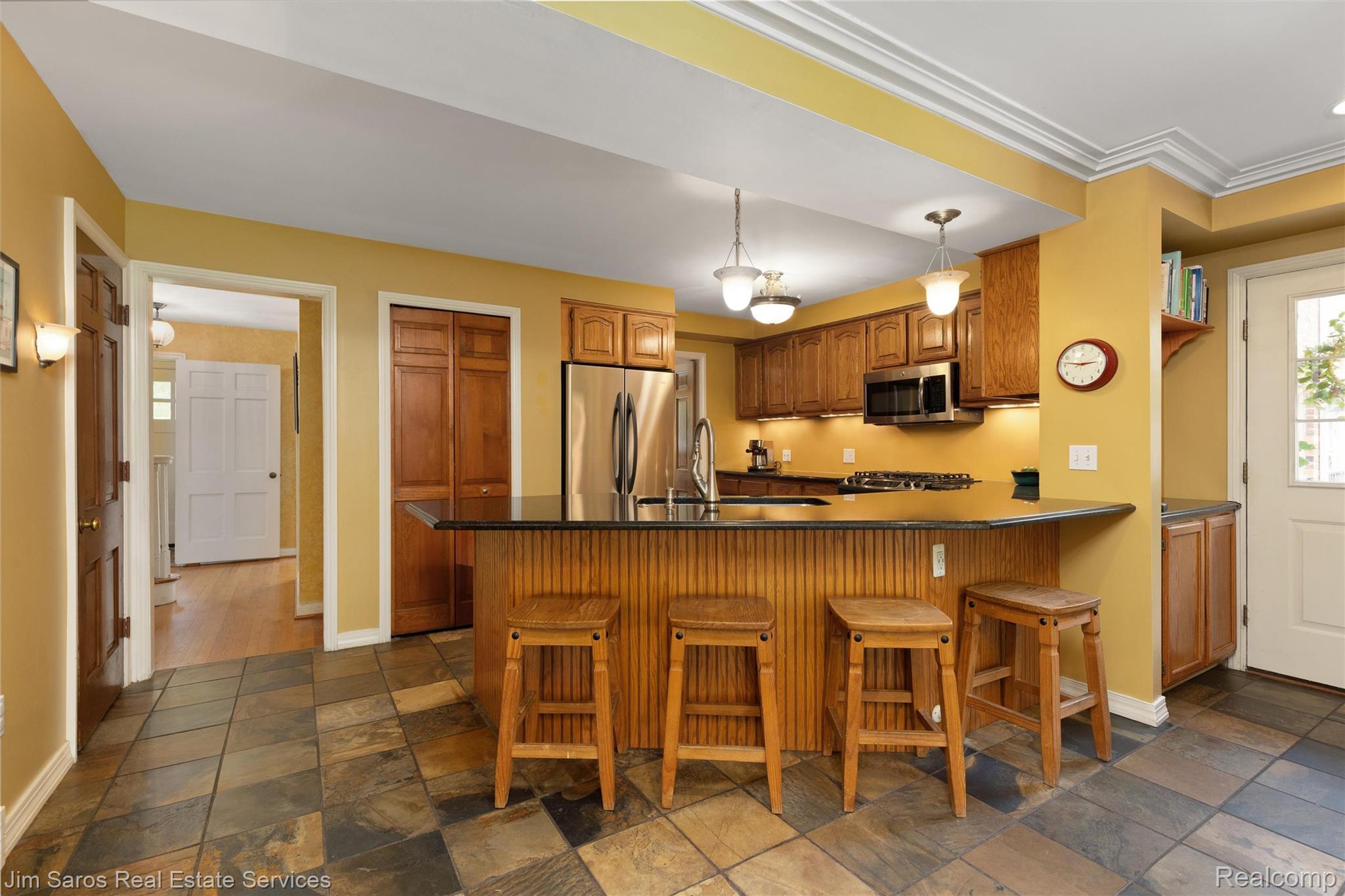 820 Westchester Road Grosse Pointe, MI 48230 - Photo 10 of 33 Kitchen with a peninsula, wood finish cabinetry, stainless steel appliances, a breakfast bar, and stone tile floors