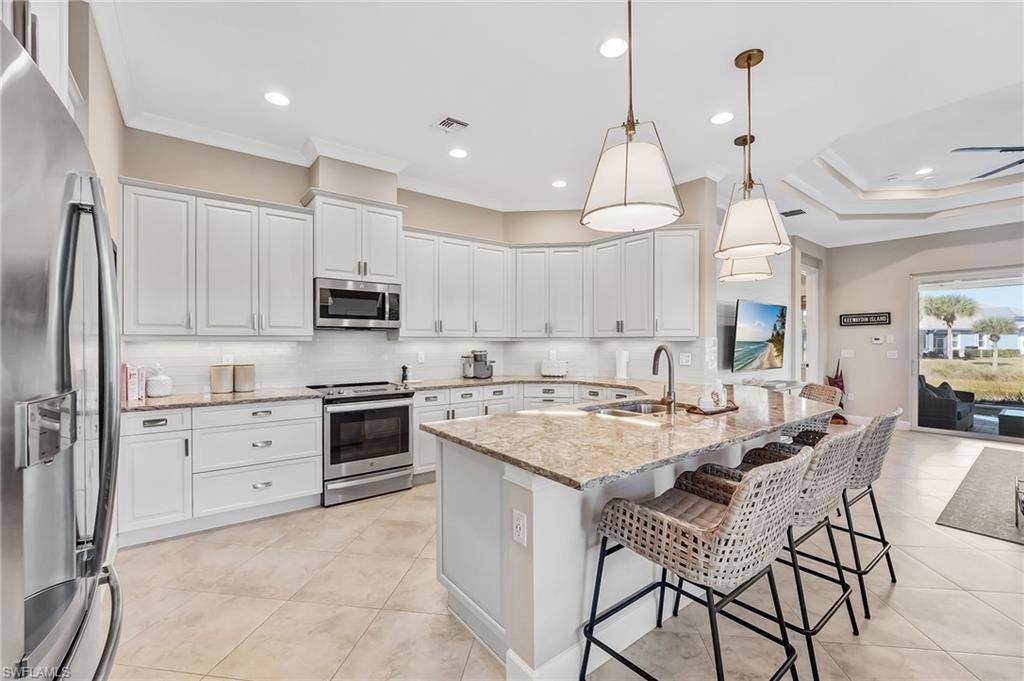 7002 Dominica Drive Naples, FL 34113 - Photo 12 of 45 Kitchen featuring appliances with stainless steel finishes, light stone counters, hanging light fixtures, a kitchen breakfast bar, and backsplash