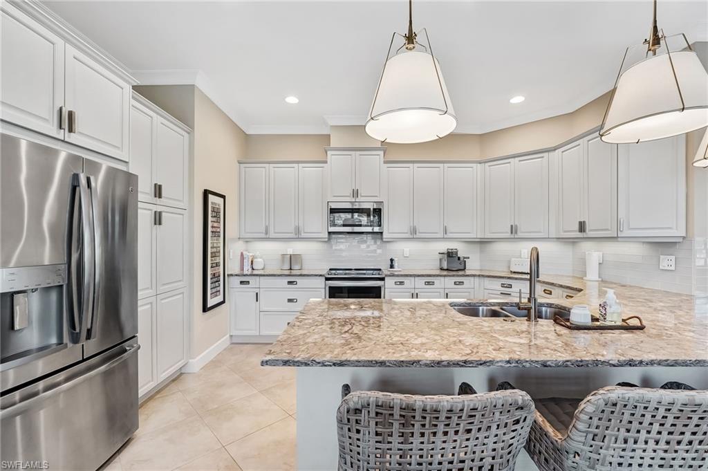 7002 Dominica Drive Naples, FL 34113 - Photo 13 of 45 Kitchen featuring stainless steel appliances, light stone countertops, a peninsula, a kitchen bar, and crown molding
