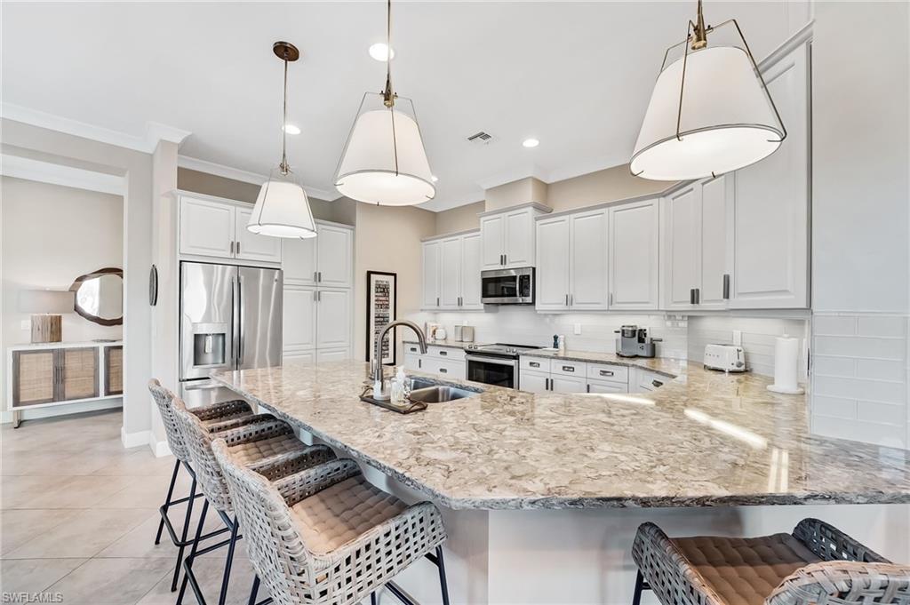 7002 Dominica Drive Naples, FL 34113 - Photo 14 of 45 Kitchen featuring a breakfast bar, a peninsula, tasteful backsplash, stainless steel appliances, and white cabinets